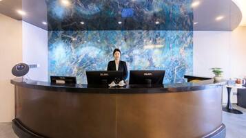 A reception desk with two laptops, a large marble wall, and a plant.