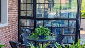 Een terras met een glazen tafel en stoelen, een plant in pot en een bakstenen muur.