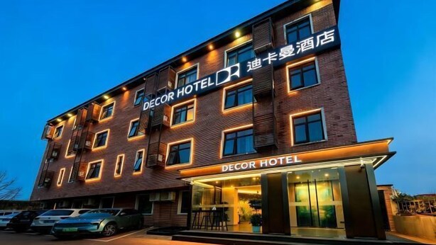 Een meerlaags hotel met een opvallend 'DECOR HOTEL' bord, een parkeerplaats met meerdere auto's en een modern architectuurontwerp.