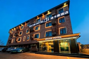 Ein mehrgeschossiges Hotel mit einem gut sichtbaren 'DECOR HOTEL' Schild, einem Parkplatz mit mehreren Autos und einem modernen architektonischen Design.