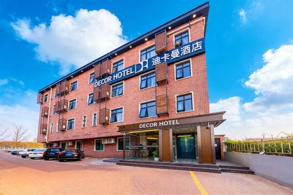 A brick building with a sign reading 'DECOR HOTEL' and a parking lot with cars.