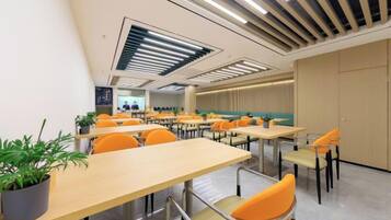 A modern classroom with rows of tables and chairs, a large screen, and a potted plant.