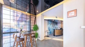 Een moderne hotellobby met een receptiebalie, een bar en een zithoek met houten stoelen en een kleine tafel.