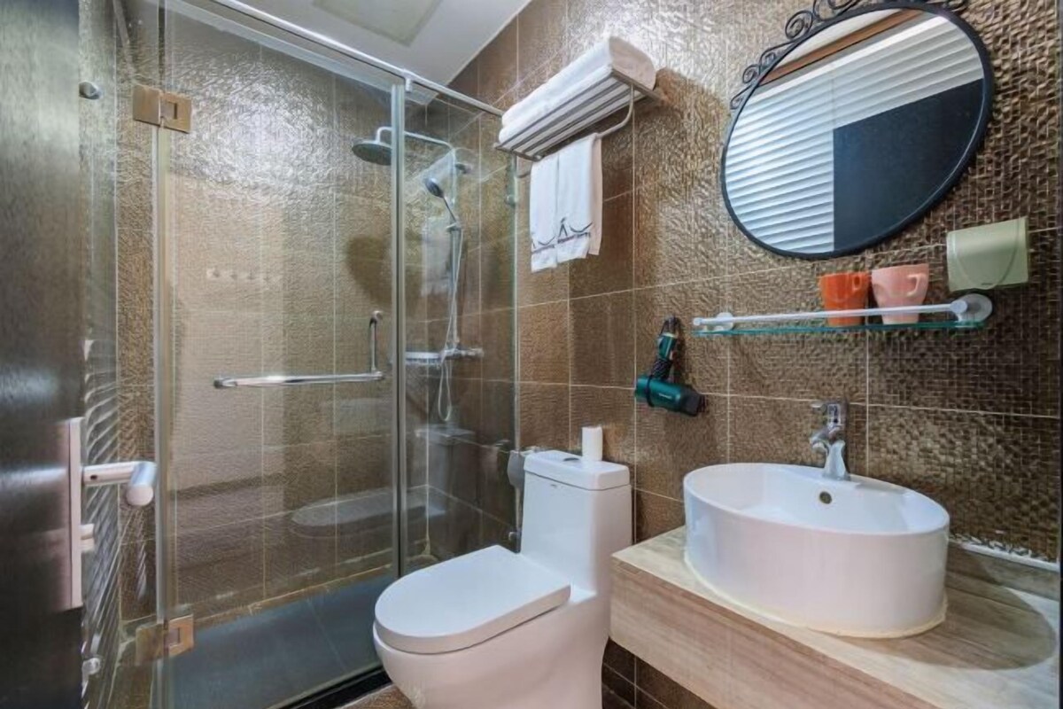 A bathroom with a glass shower enclosure, a toilet, a sink, a mirror, and a towel rack.