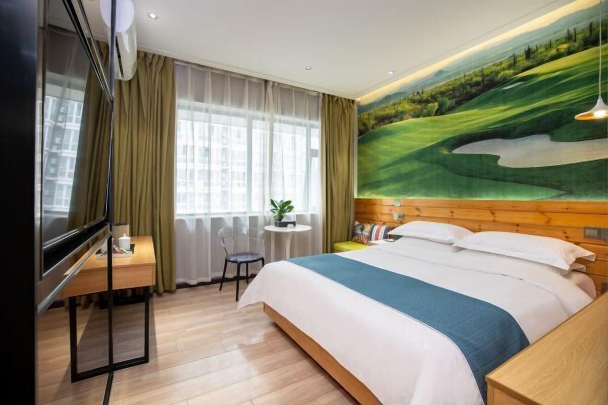 Ein Hotelzimmer mit einem Bett, einem Schreibtisch, einem Stuhl, einem Fernseher und einem großen Gemälde an der Wand.