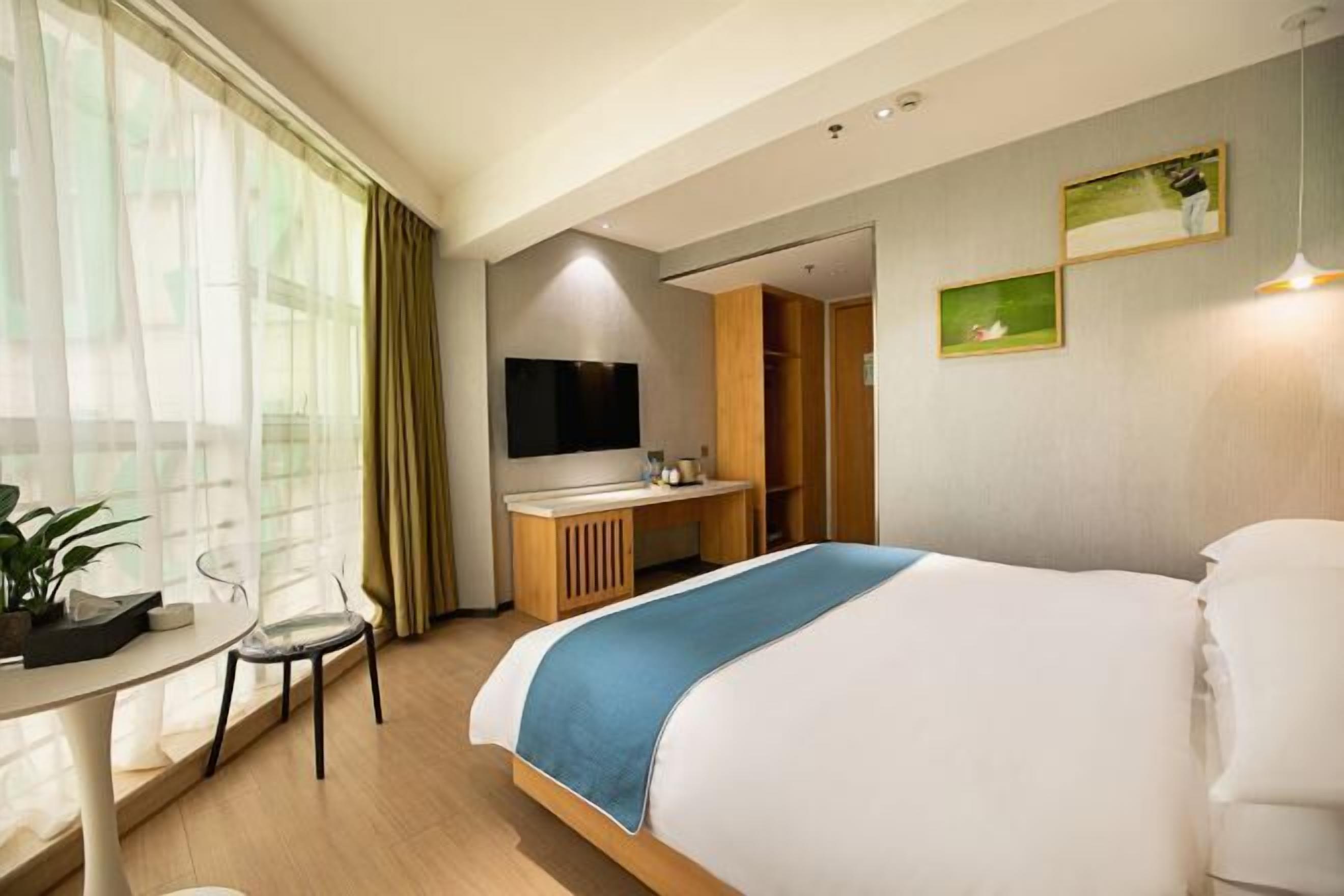 A hotel room with a bed, a desk, a chair, a TV, and a wardrobe.