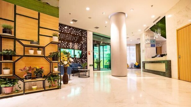 Eine moderne Hotelhalle mit Empfangsschalter, einer großen Säule sowie einer Wand mit geometrischen Regalen und Topfpflanzen.