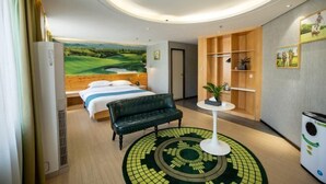 Ein Hotelzimmer mit einem Bett, einem Schreibtisch, einem Sessel und einem runden Teppich. An der Wand hängt ein Bild einer Golfanlage.