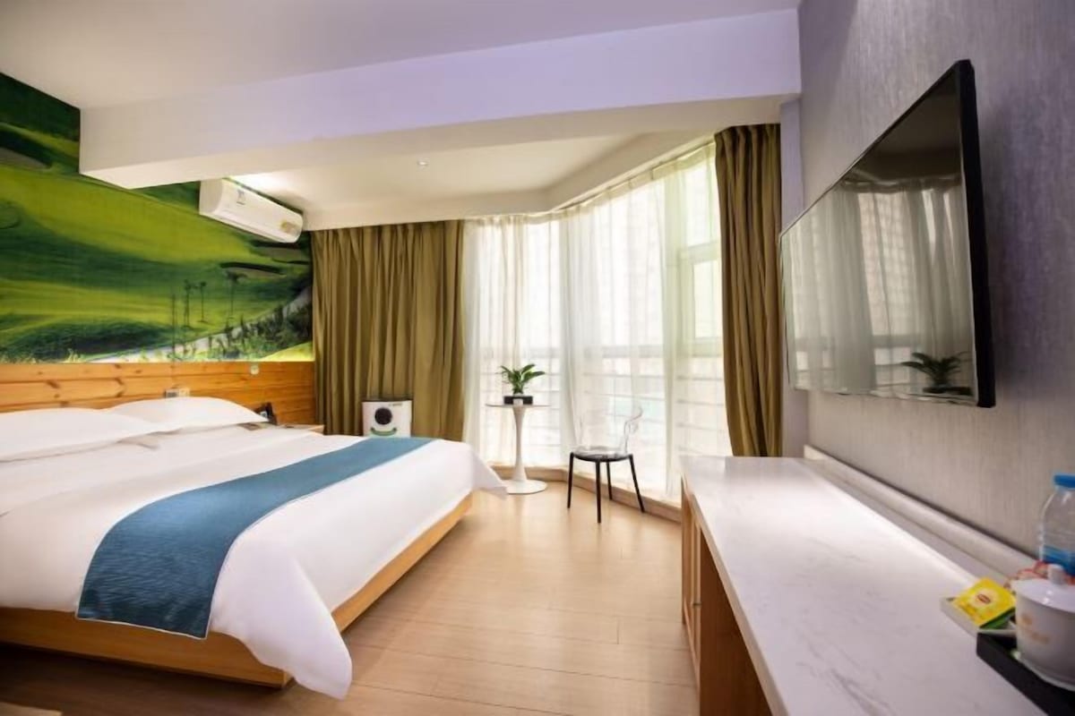 Ein Hotelzimmer mit Bett, Schreibtisch, Stuhl, Fernseher und einem Fenster mit Vorhängen.