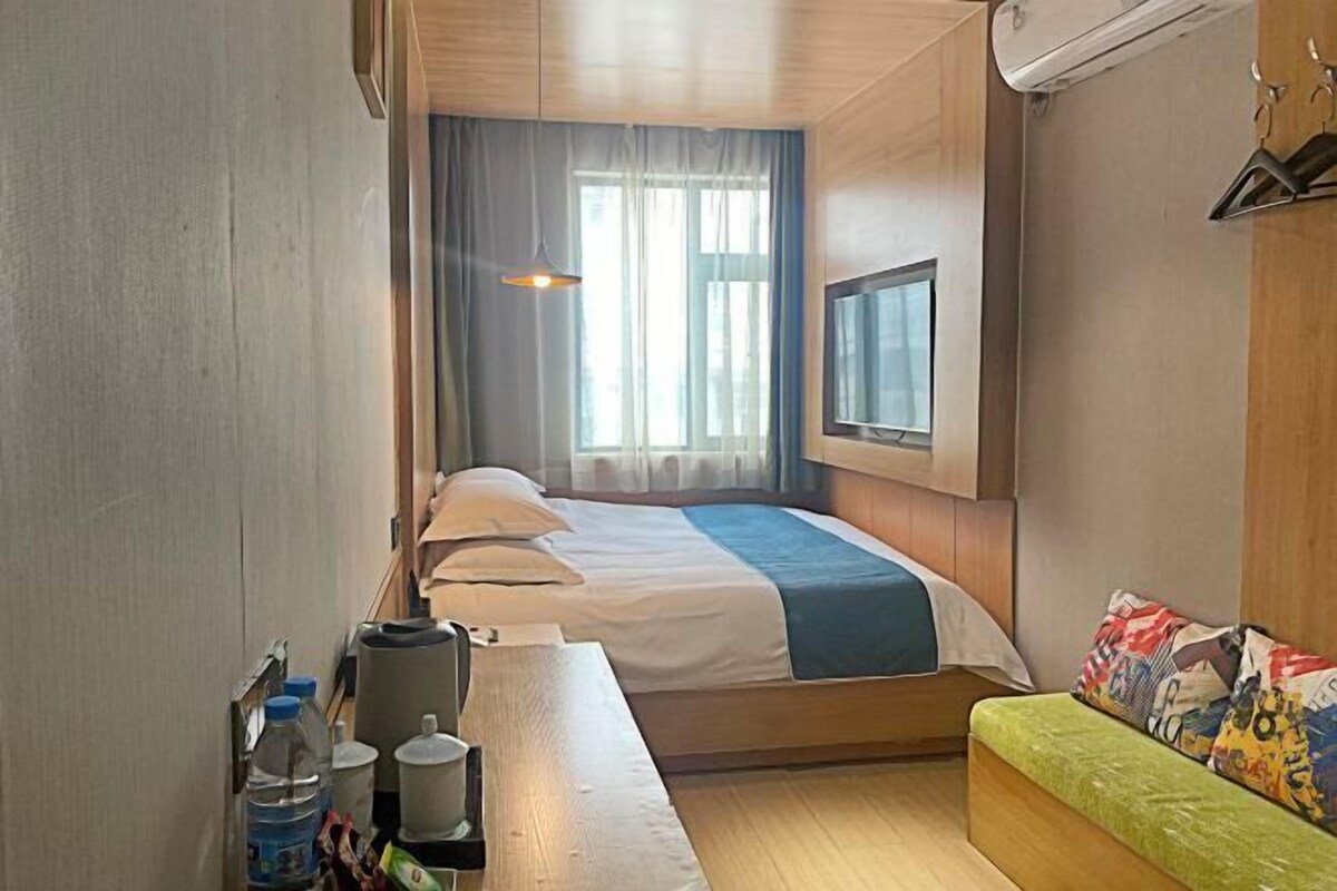 Ein Hotelzimmer mit einem Bett, einer Bank, einem Fenster und einem an der Wand befestigten Fernseher.