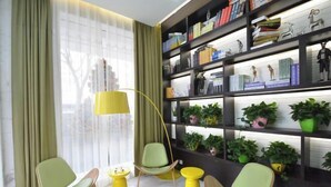 Ein modernes Wohnzimmer mit grünen Sesseln, gelben Beistelltischen und einem Bücherregal voller Bücher und Dekoration.