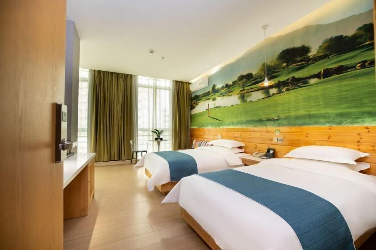 Ein Hotelzimmer mit zwei Betten, einem Holzkopfende, einem großen Fenster mit Vorhängen und einem Landschaftsbild.