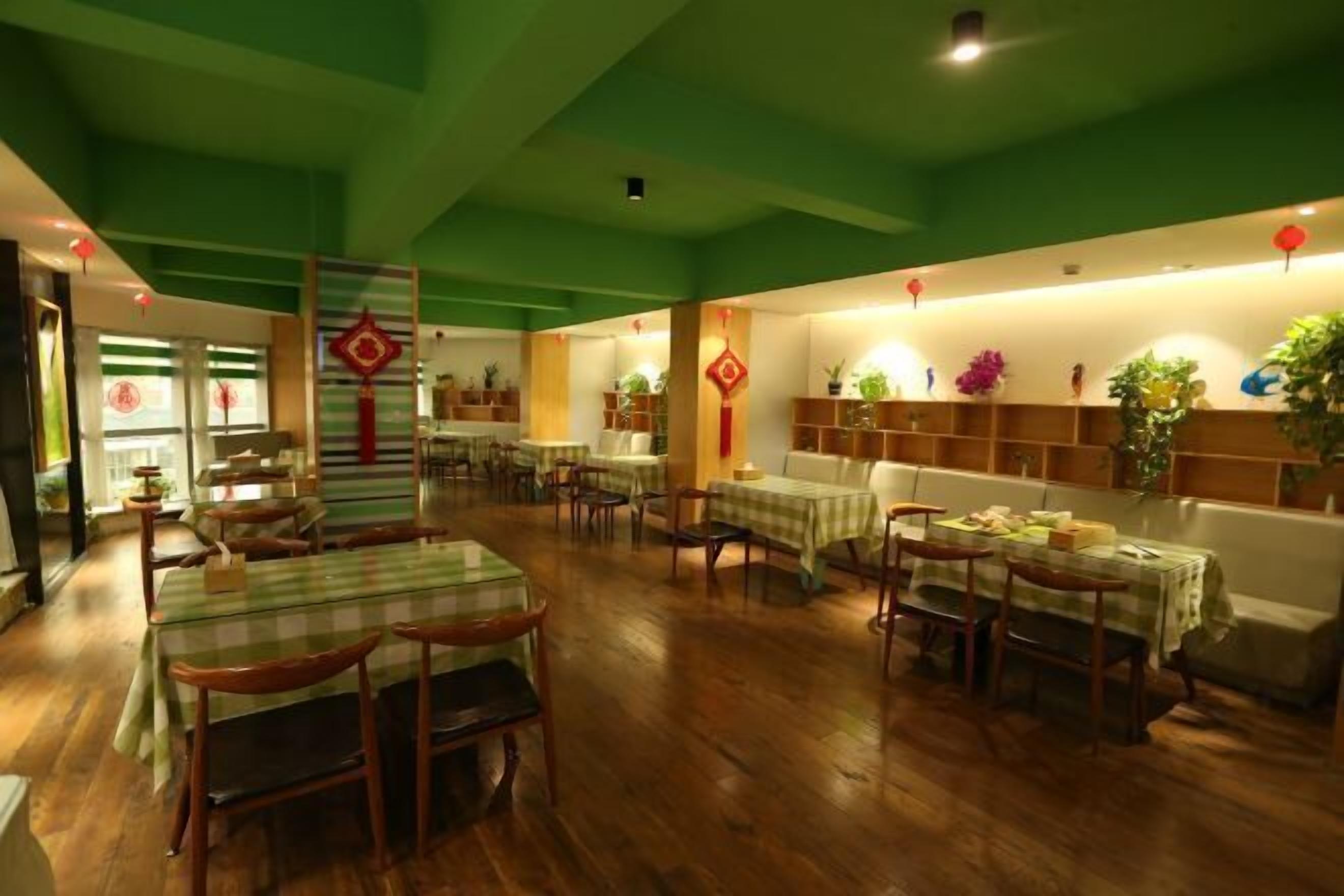 Een restaurant met houten tafels en stoelen, groene wanden en rode decoraties.