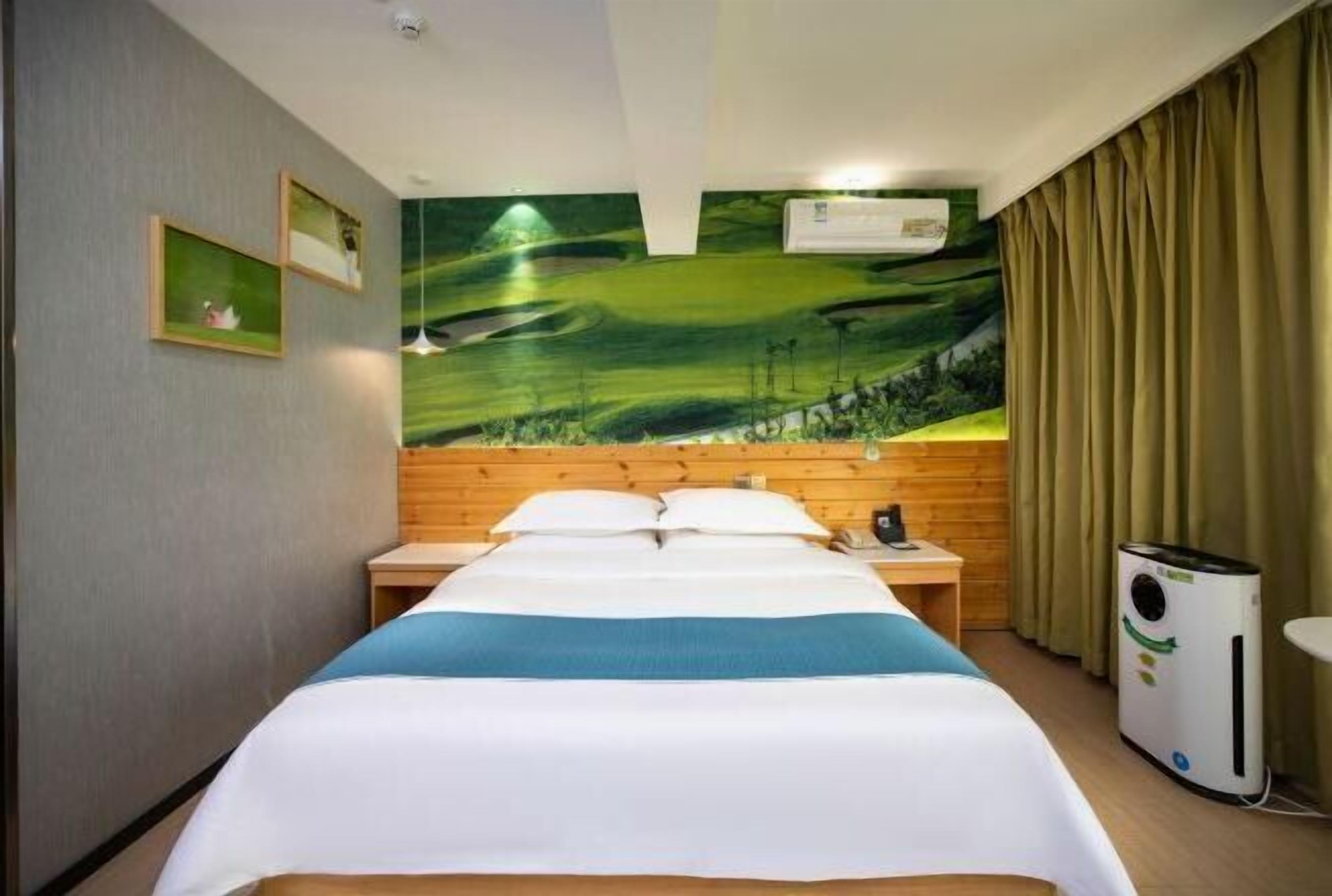 A hotel room with a bed, wooden headboard, a wall mural, a window with curtains, and a heater.