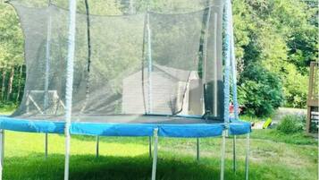 A trampoline with a safety net enclosure in a grassy area with trees in the background.