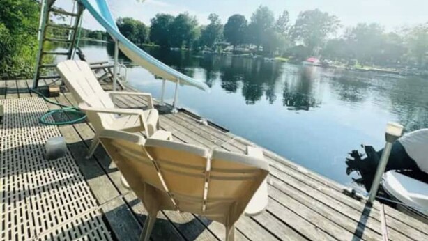 A wooden deck with lounge chairs and a slide over a body of water. - Beautiful Waterfront Cottage with Hot Tub in South Muskoka  (Severn Bridge)