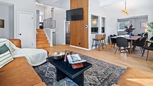 A modern living room with a sofa, coffee table, and a dining area with chairs and a table. - Hot Tub - Game Room - Sleeps 10 - Akron (Akron)