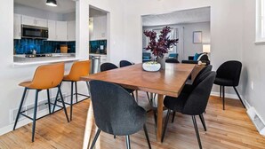 A modern dining area with a wooden table and chairs, a chandelier, and a kitchen visible through an open archway. - Hot Tub - Game Room - Sleeps 10 - Akron (Akron)