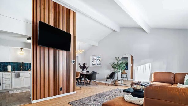 A modern living room with a brown leather sofa, a wooden accent wall, and a flat-screen TV mounted above it. - Hot Tub - Game Room - Sleeps 10 - Akron (Akron)