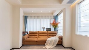 A modern living room with a beige sofa, a white rug, and a large window with blinds. - Guiyu·Yin (Hangzhou)