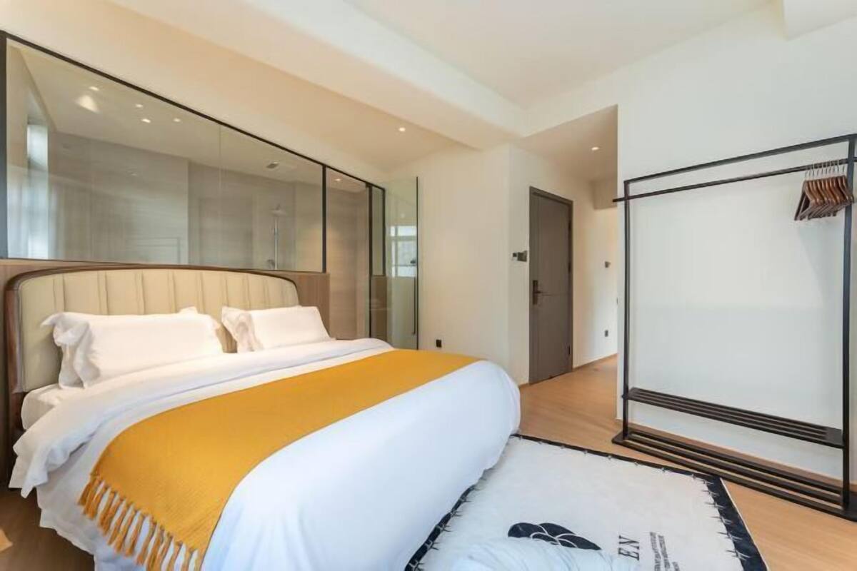 A modern hotel room with a large bed, a mirror, a wardrobe, and a wooden floor.