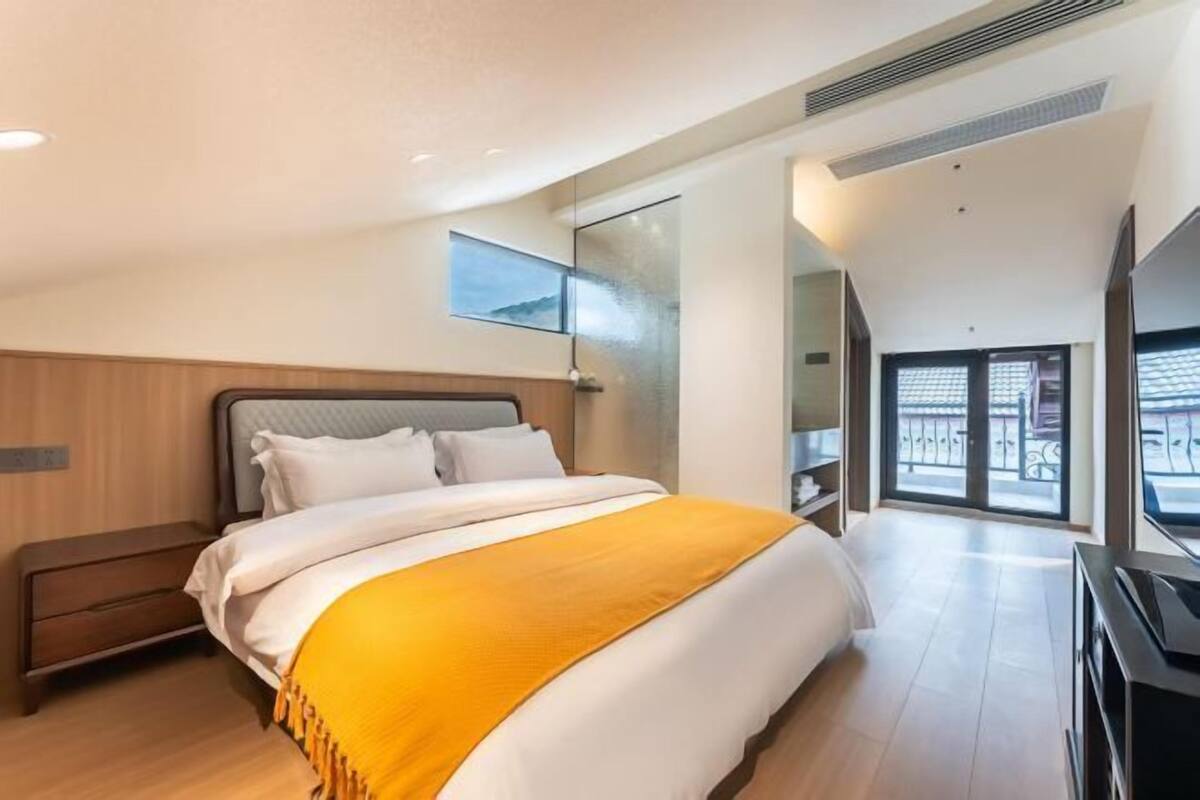 A modern hotel room with a large bed, a TV, and a balcony with a view.