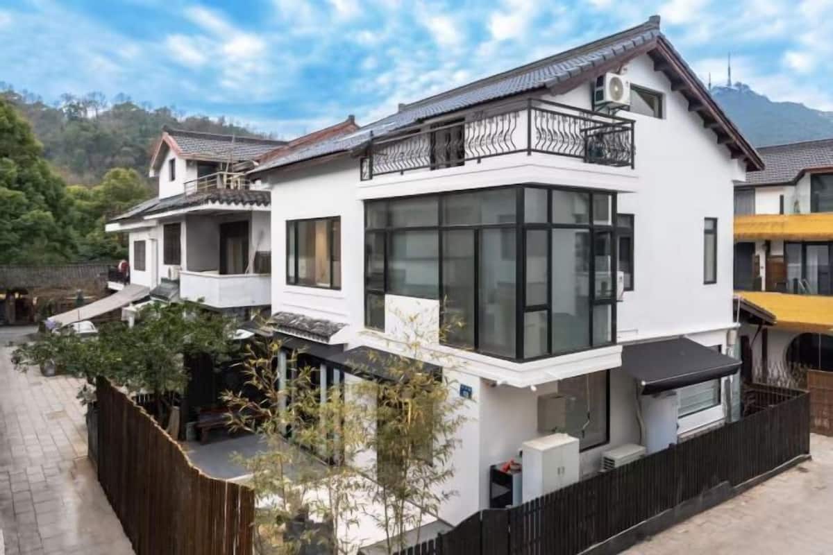 A modern two-story house with large windows, a balcony, and a fenced yard.