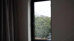 A window with a view of a dense green hedge and a building in the background. - Guiyu·Yin (Hangzhou)