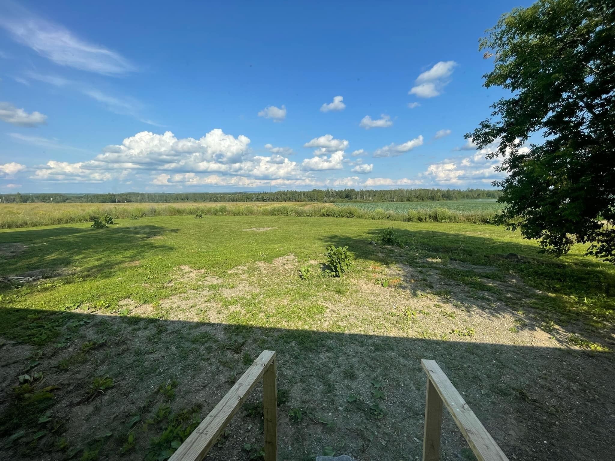 Un paysage rural avec un ciel dégagé, un chemin de terre et une structure en bois au premier plan.