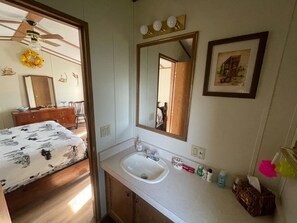 A bedroom with a bed, a dresser, a vanity with a mirror, and a bathroom with a sink and toiletries.