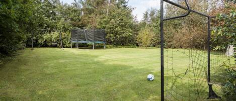 Een gazon met een voetbaldoel, een trampoline en een schommel.