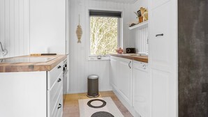 A compact kitchen with white cabinetry, a wooden countertop, a window with a view of trees, and a small trash bin. - Pet friendly home in Spøttrup with WiFi (Spøttrup)