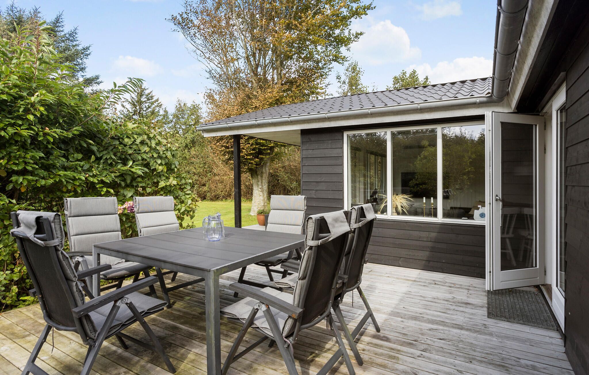 An outdoor patio with a table and chairs, a small covered area with a window, and a wooden deck.