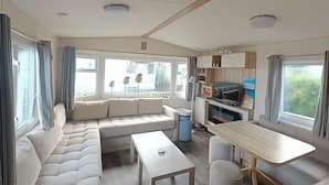 L’intérieur d’une caravane, avec un canapé, une table, un téléviseur et une fenêtre avec des rideaux.