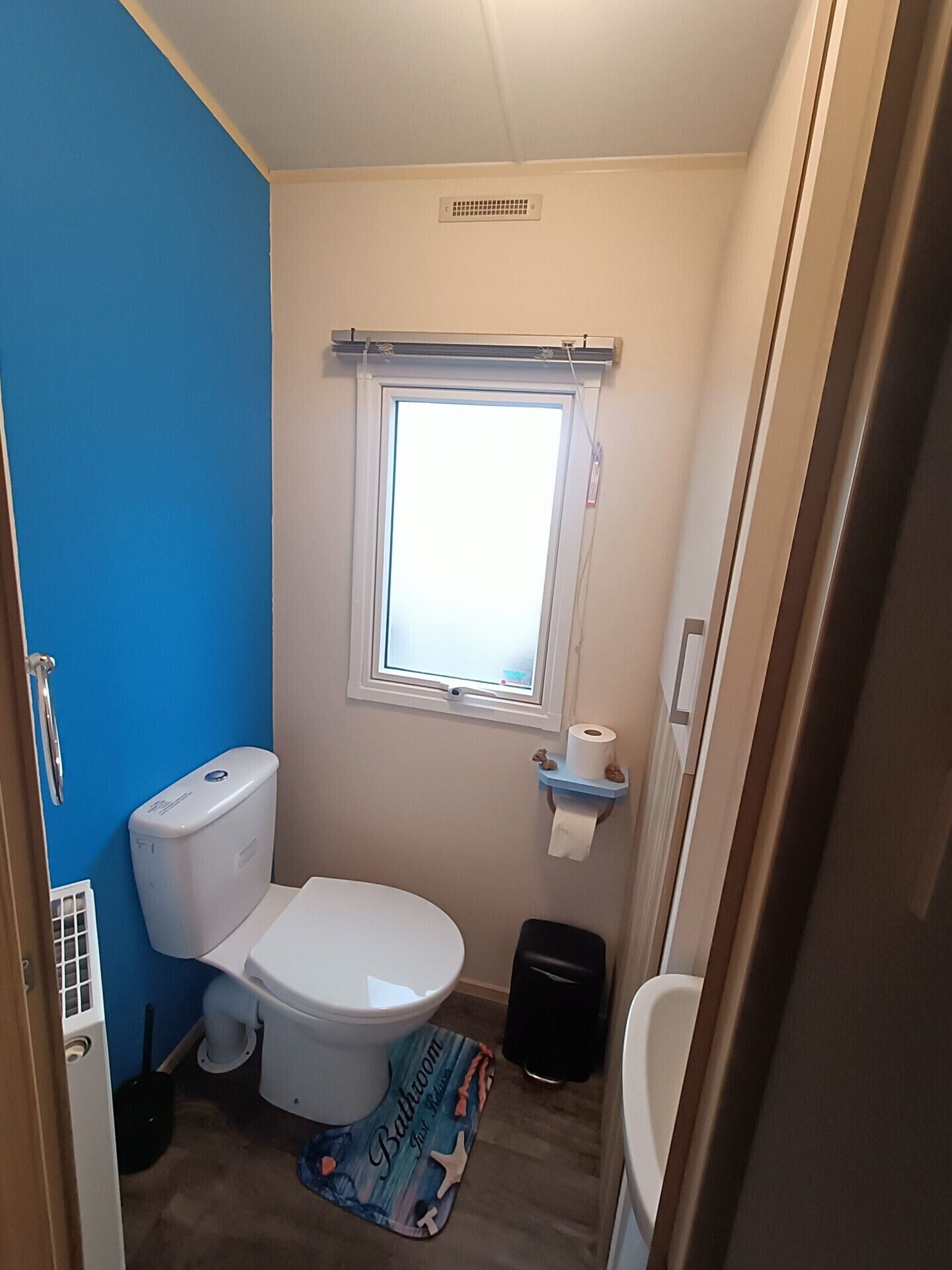 A small bathroom with a toilet, a window, and a blue wall.