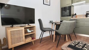 A modern kitchen with a flat-screen TV, wooden furniture, and a dining area with chairs. - L'Olivier -4prs/ T2/Pontivy (Pontivy)