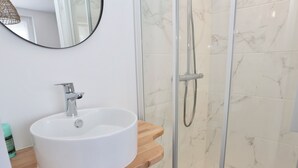 A bathroom with a white sink, a wooden vanity, a glass shower enclosure, and marble tiles. - L'Olivier -4prs/ T2/Pontivy (Pontivy)