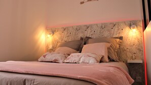 A neatly made bed with a pink blanket, a wall-mounted light fixture, and a decorative arrow sign. - Le Flamingo - Wifi - 400m centre Pontivy (Pontivy)