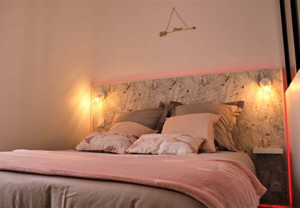 A neatly made bed with a pink blanket, a wall-mounted light fixture, and a decorative arrow sign.