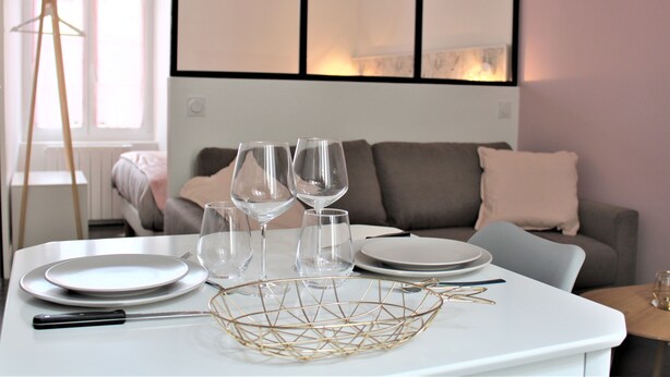 A dining table set with plates, glasses, and cutlery in a modern room with a sofa and a window. - Le Flamingo - Wifi - 400m centre Pontivy (Pontivy)