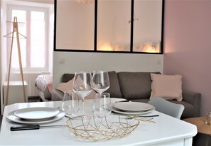 A dining table set with plates, glasses, and cutlery in a modern room with a sofa and a window.