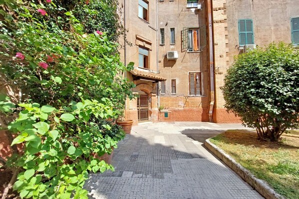 Une ruelle étroite bordée d’un immeuble en briques, d’une plante en pot et d’un petit arbre.