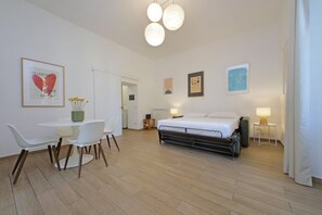 A modern hotel room with a bed, bedside tables, a desk with chairs, and artwork on the walls.