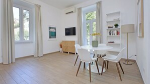 A modern living room with a round dining table, white chairs, a sofa, a TV, and a bookshelf. - Cozy and recently renovated apartment for 4 near the Vatican (Roma)