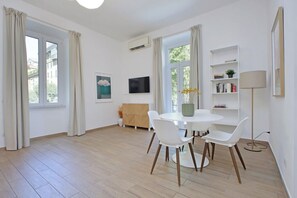 Un salon moderne avec une table de salle à manger ronde, des chaises blanches, un canapé, un téléviseur et une bibliothèque.
