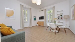 A modern living room with a grey sofa, a dining table with chairs, a flat-screen TV, and a bookshelf. - Cozy and recently renovated apartment for 4 near the Vatican (Roma)