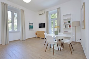 A modern living room with a round dining table, white chairs, a sofa, a TV, and a bookshelf.