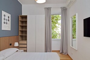 A bedroom with a bed, a wardrobe, a bedside table, a lamp, and a window with curtains.