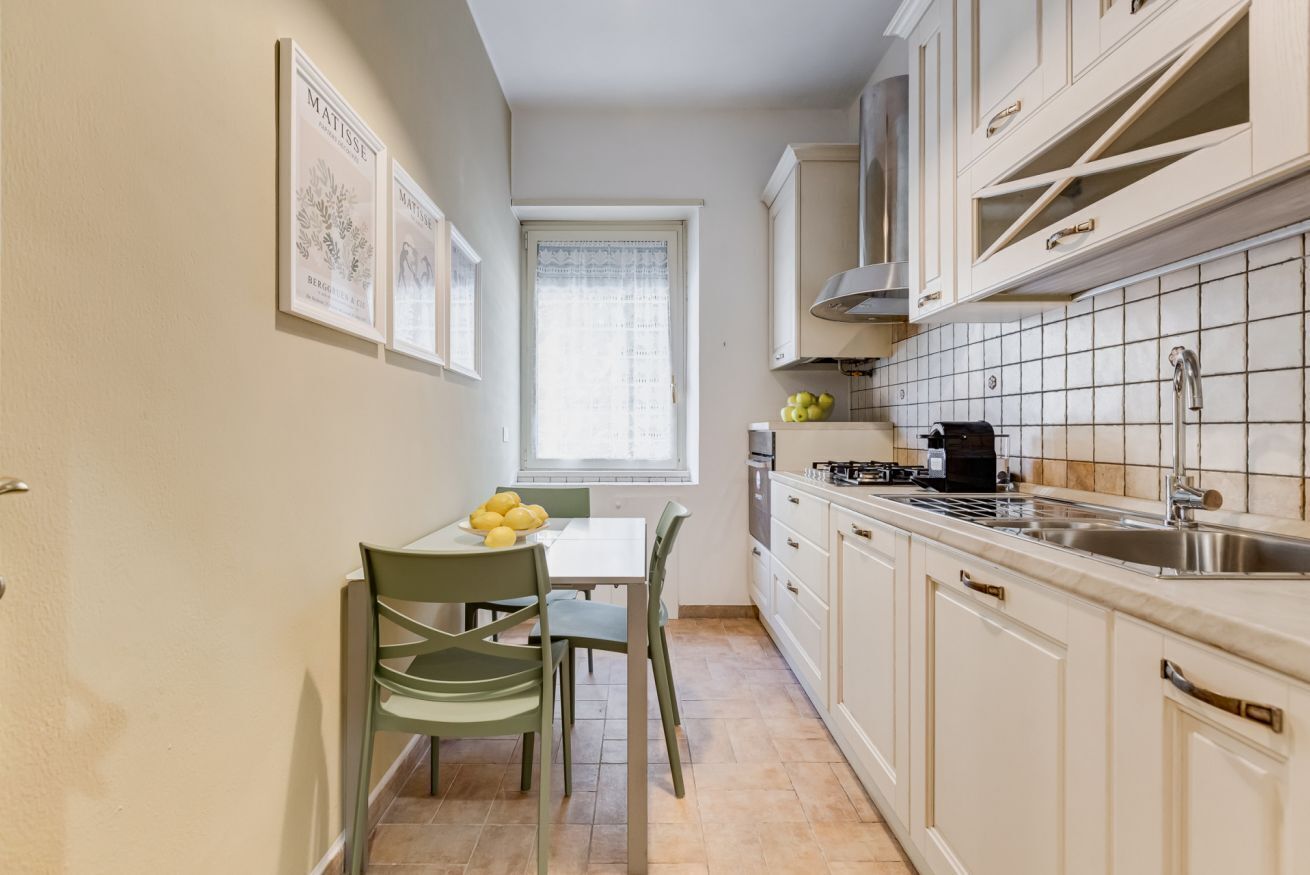 A compact kitchen with white cabinets, a dining table with chairs, and a window with a curtain.