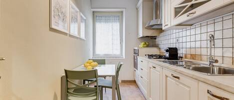 A compact kitchen with white cabinets, a dining table with chairs, and a window with a curtain.